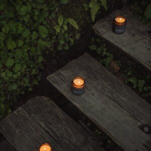 Warm lit candles arranged on wooden steps surrounded by green foliage for a cozy ambiance.