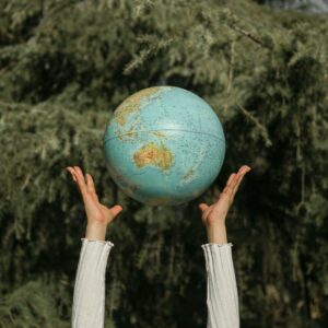 Hands raising a globe against a lush green tree backdrop, symbolizing environmental awareness.