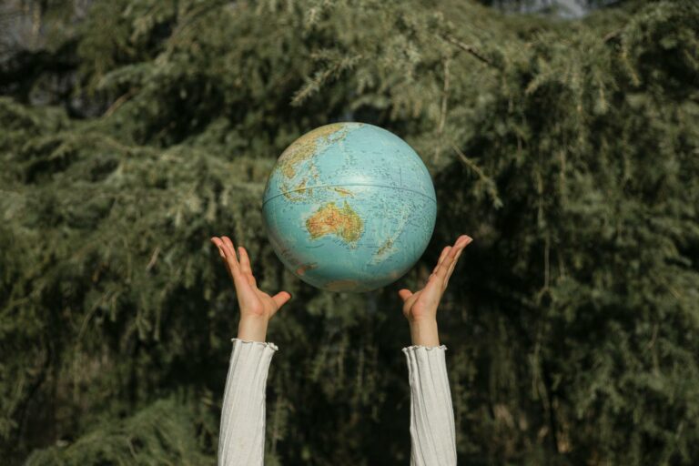 Hands raising a globe against a lush green tree backdrop, symbolizing environmental awareness.