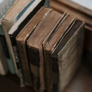 A vertical close-up capturing a collection of old, worn books on a wooden surface.