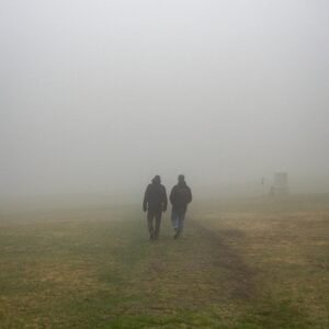 a couple of people walking across a grass covered field